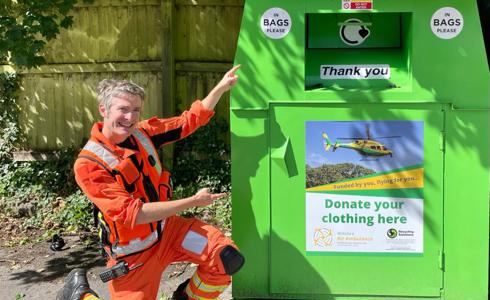 A doctor wearing an orange flight suit, crouched and pointing at a WAA green clothing bank