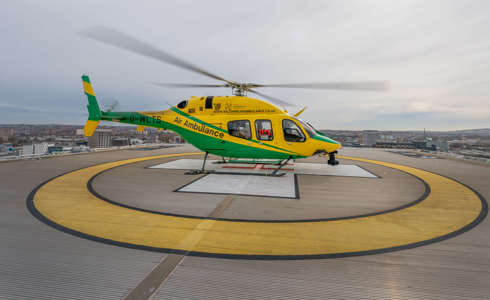 The yellow and green helicopter landed with its rotor blades turning on a hospital helipad on a grey day.