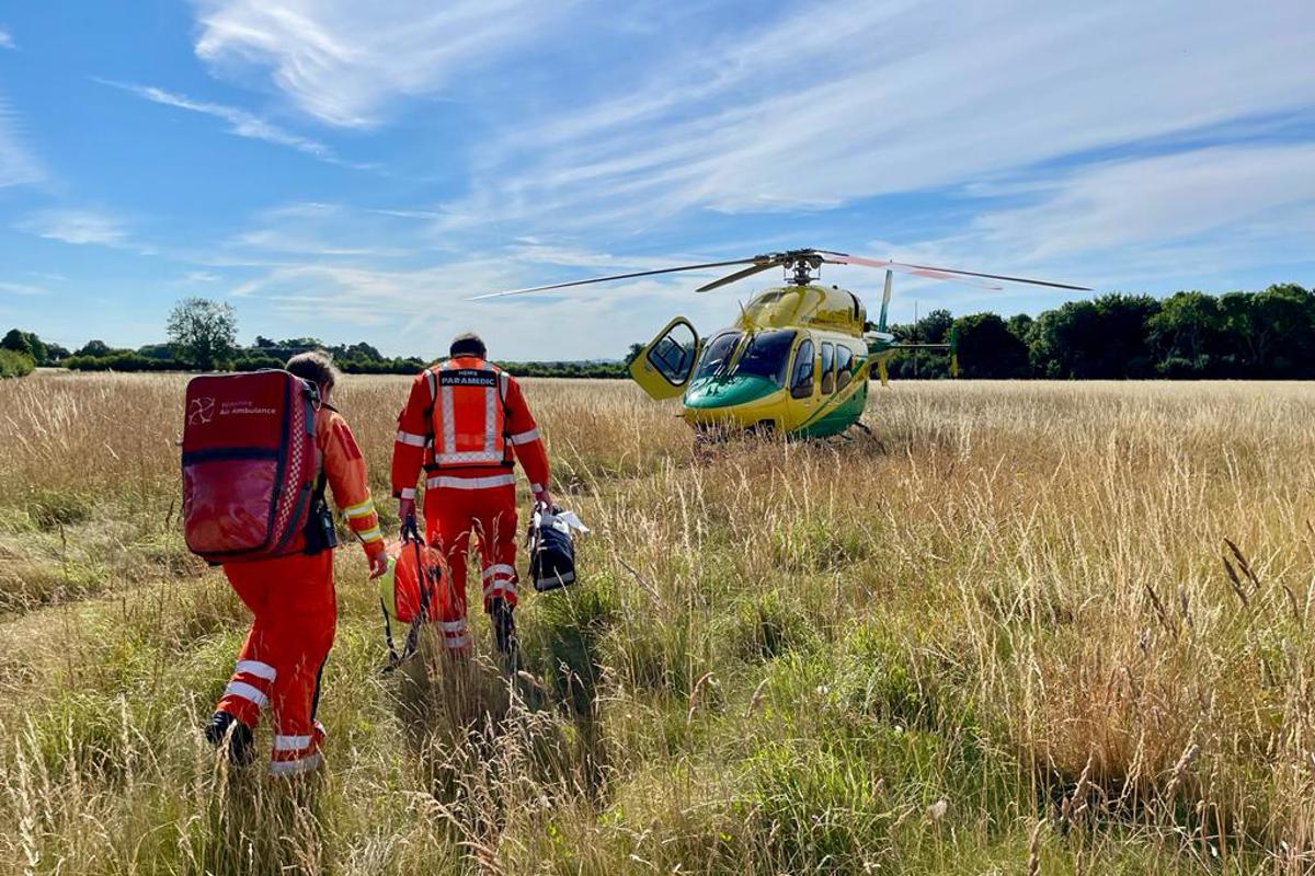 A photo of two paramedics, carrying kit bags, walking through long grass to the helicopter